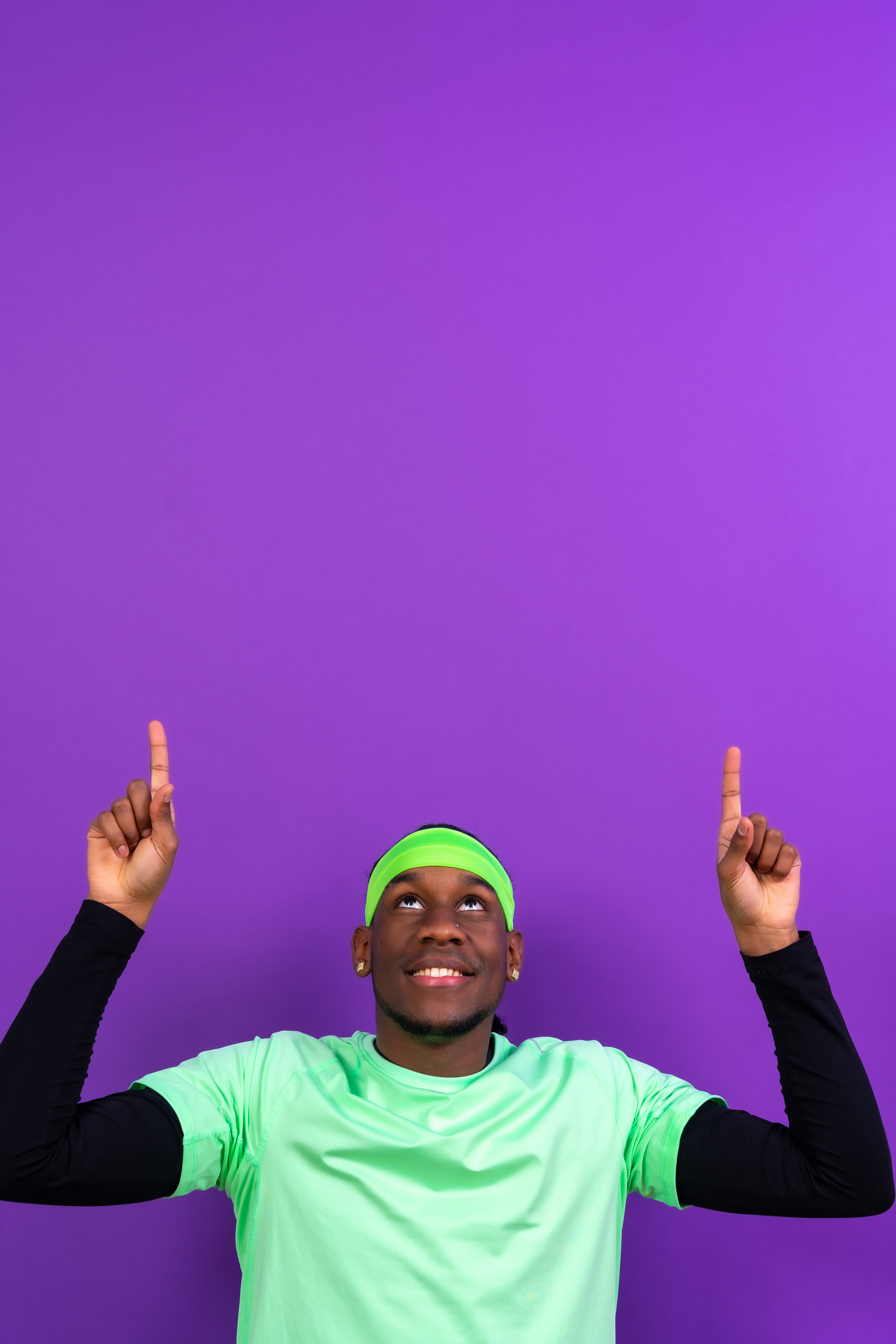 Black ethnic man in green clothes on a purple background, pointing to a free copy space above, vertical photo